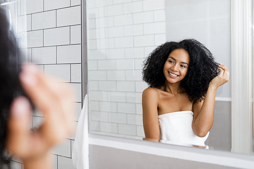 Young woman standing in bathroom, holding her curly hair