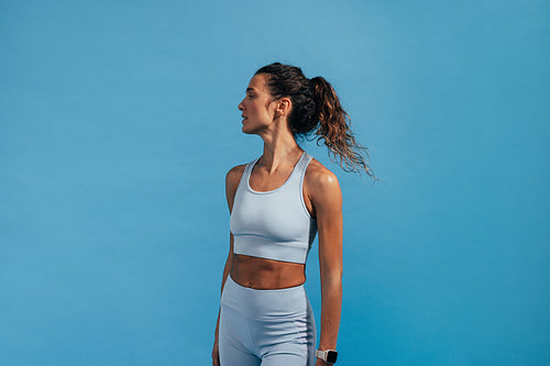 Side view portrait of sportswoman in blue fitness wear. Female athlete standing on blue background.