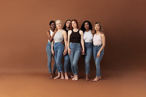 Six women of different ages standing together in studio. Females holding hands and looking at camera.