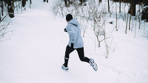 Rear view of young athlete running at path in forest