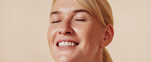 High-detailed portrait of a smiling female with freckles. Happy blond with closed eyes and freckled skin.