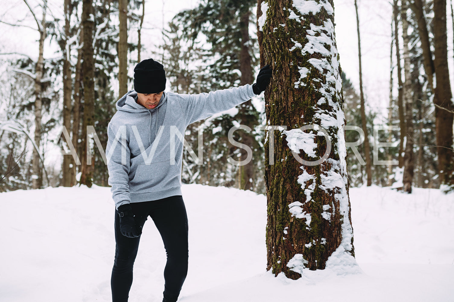 Tired athlete standing near a tree and resting after workout, looking down	
