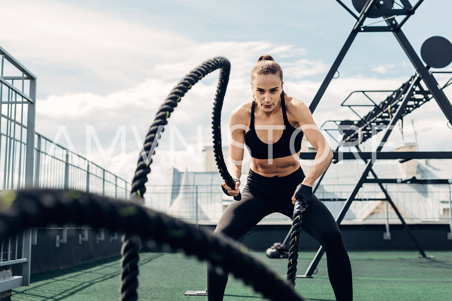 Woman in fitness wear working out with two battle ropes on rooftop	
