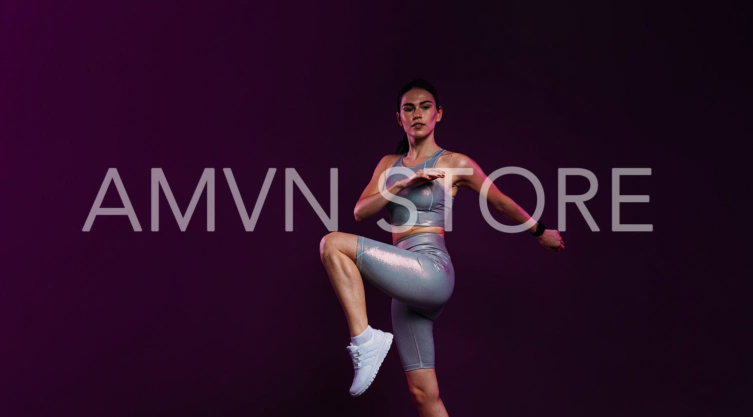 Slim woman in silver fitness clothes warming up her legs in studio against magenta backdrop