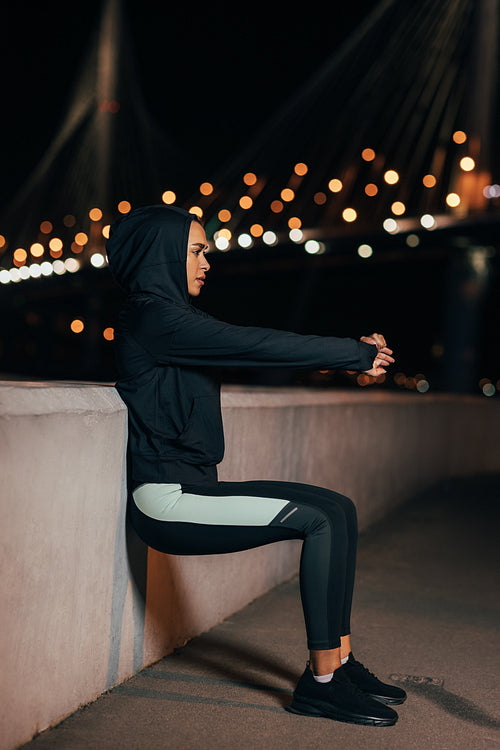 Side view of a young fit woman doing wall squat. Sportswoman doing wall sit at night.