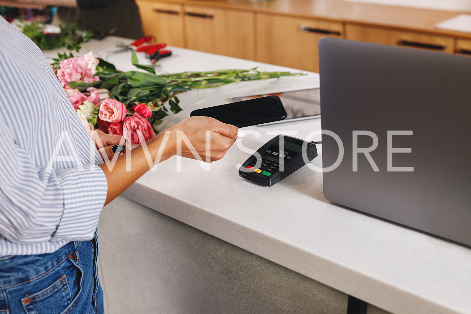 Hand of a woman with smartphone making contactless payment at flower shop.	