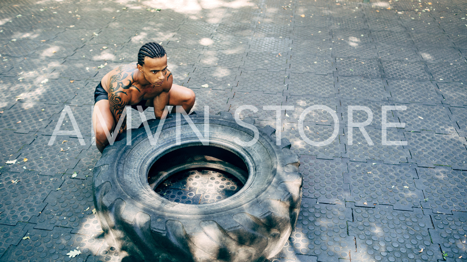 Muscular man doing squats with huge tire on sports ground outdoors	