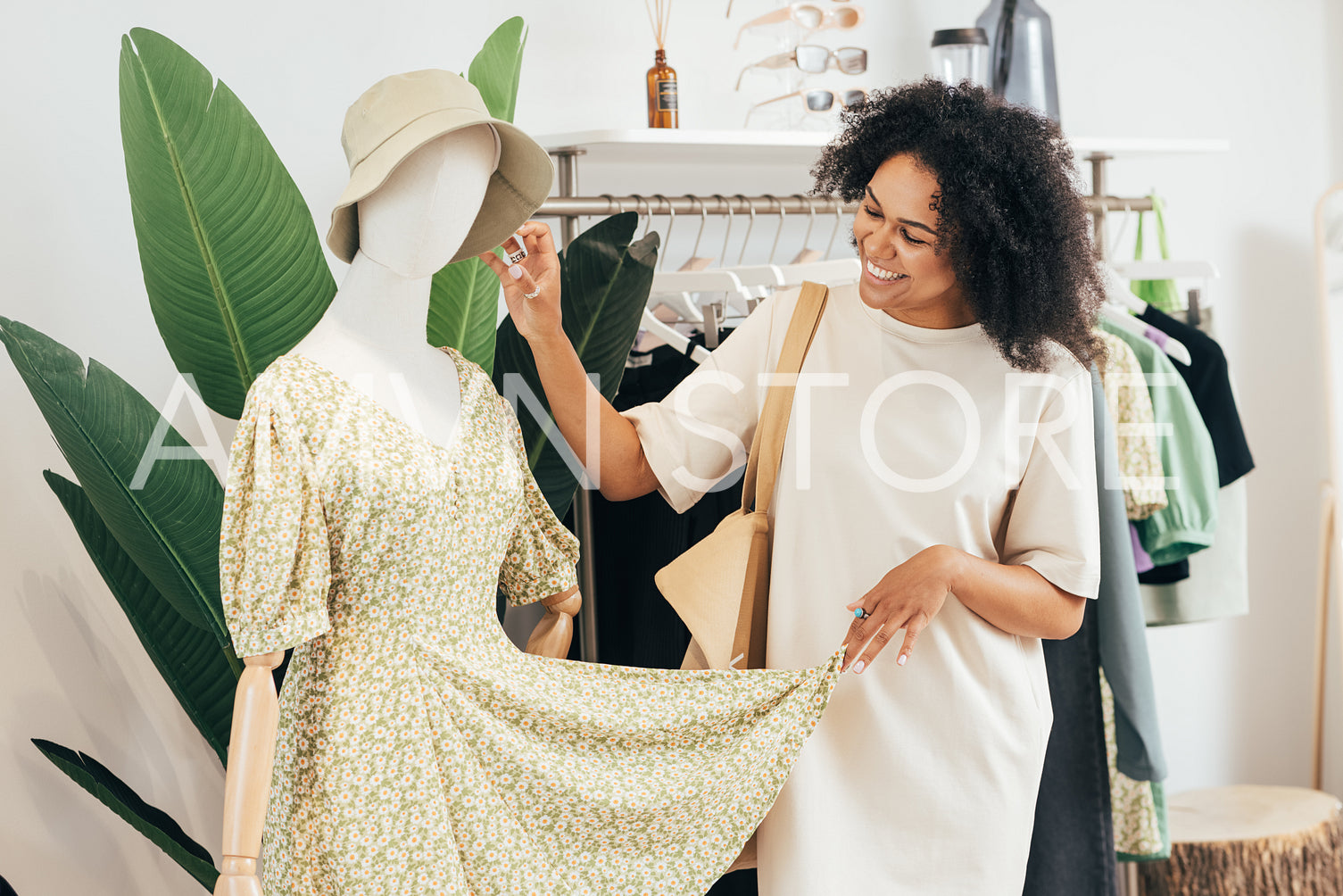 Cheerful stylish woman looking at clothes on a mannequin. Young female buying new clothes in a boutique.