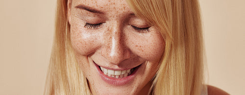 Cropped highly detailed shot of positive female with freckles. Close-up portrait of young woman with closed eyes and freckled skin over pastel backdrop.