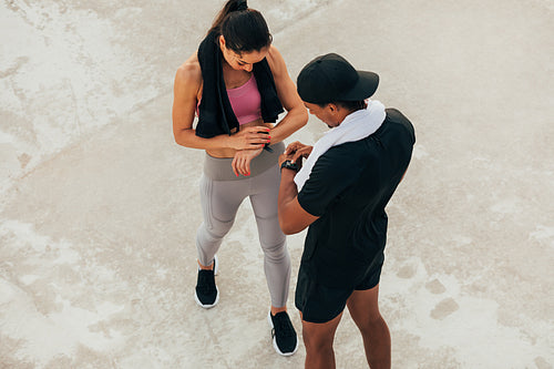 Shot from above on two athletes checking their smartwatch after training. Fitness couple adjusting fitness trackers.