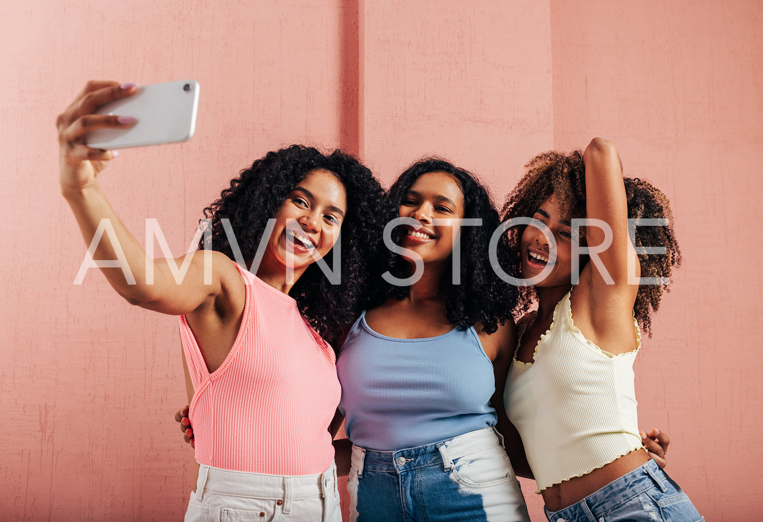 Three happy women with curly hair taking selfie against pink wall