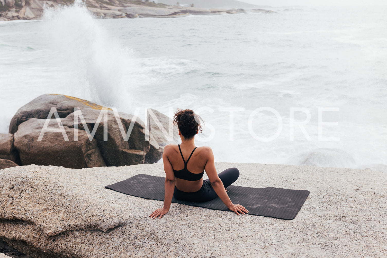 Back view of fit female sitting on a mat and looking at waves 