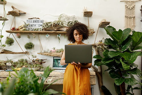 Young woman standing with laptop in her botanical studio