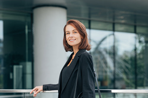 Smiling woman with ginger hair in black formal clothes outdoors