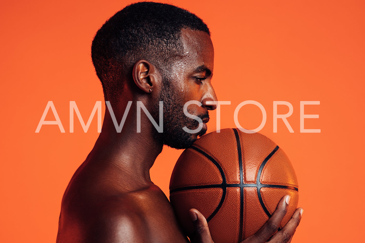 Side view of sportsman with basket ball under his chin against orange background in studio