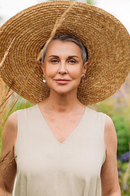 Portrait of a mature female in big straw hat standing outdoors in the field