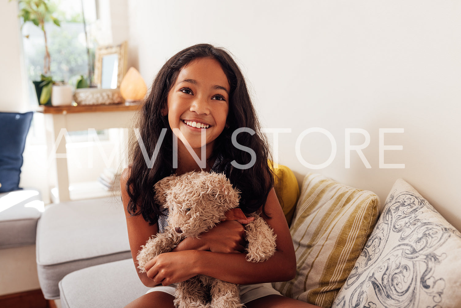 Portrait of a happy girl sitting on a sofa in living room hugging teddy bear