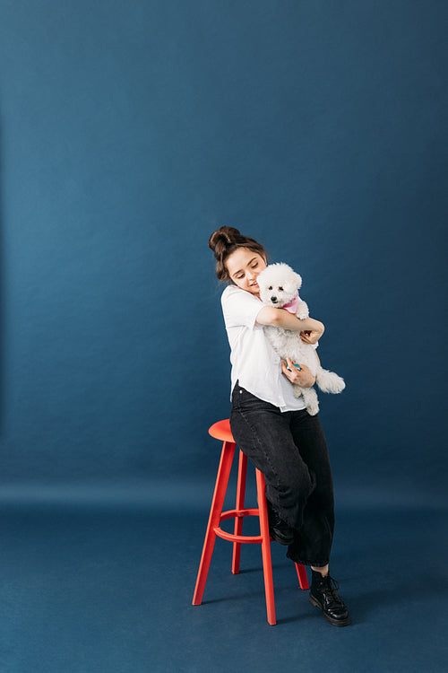 Pet parent hugging her little fluffy dog while sitting on chair