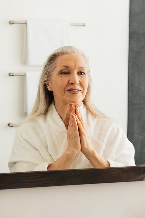 Senior woman in bathrobe admires her reflection in a bathroom mirror