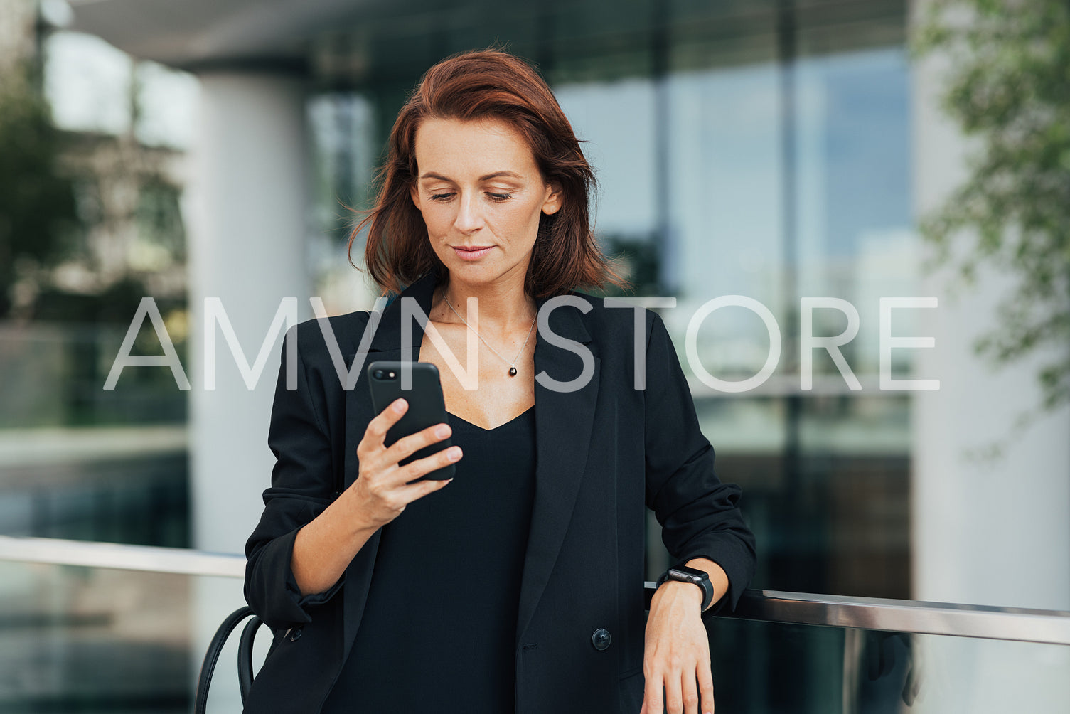 Middle-aged businesswoman in black formal wear looking at her smartphone while standing outdoors