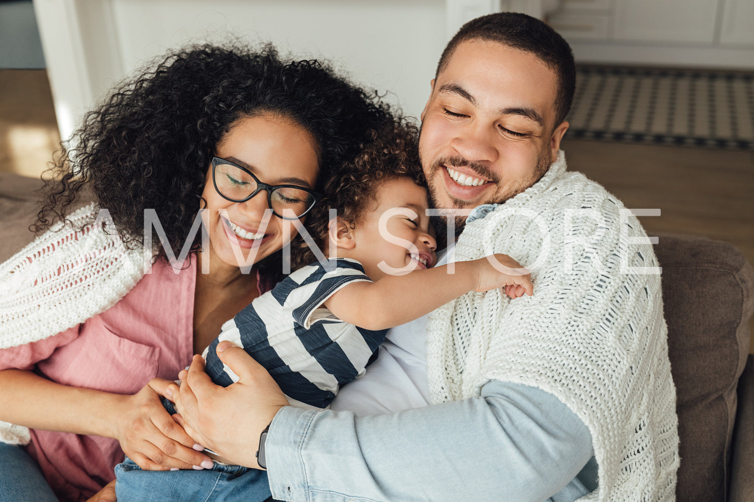 Happy family sitting on a couch at home. Mother, father, and their son embracing