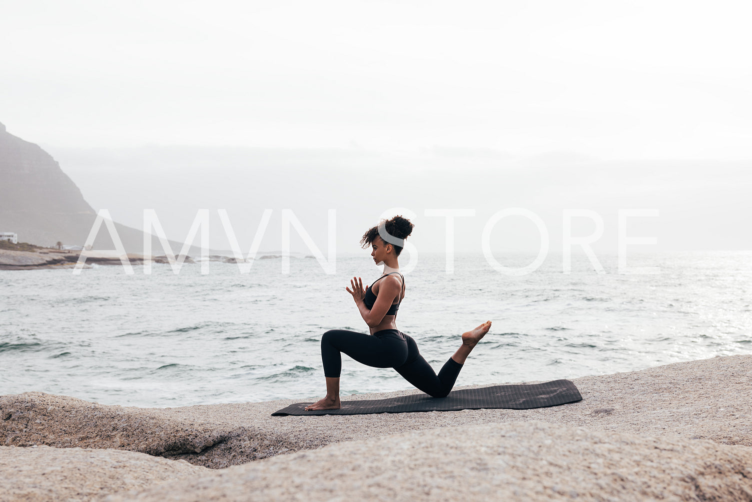 Side view of fit woman practicing yoga on mat by ocean. Female meditating at evening with folded hands.