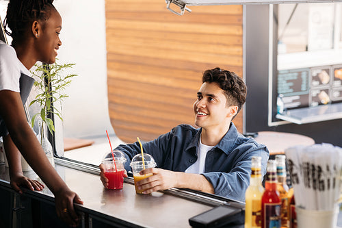 Young man holding juice on a counter of food truck looking at saleswoman