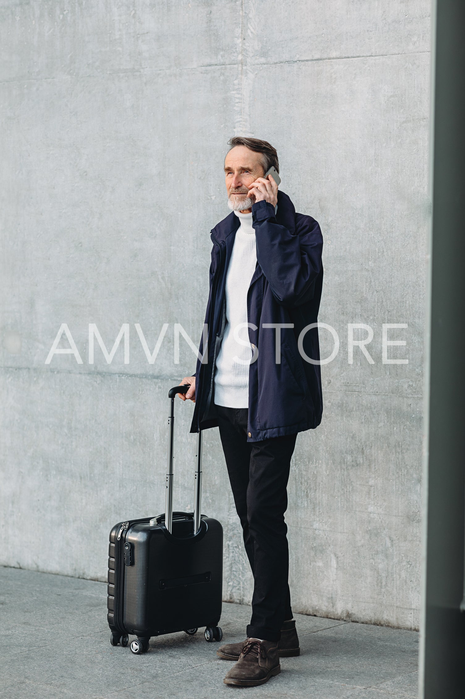 Traveler standing outdoors with suitcase and making call on cell phone	