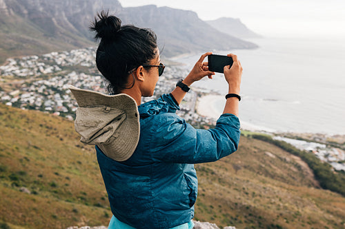 Young woman taking photographs with her smartphone while hiking on a mountain. Female hiker making photos for her social media.