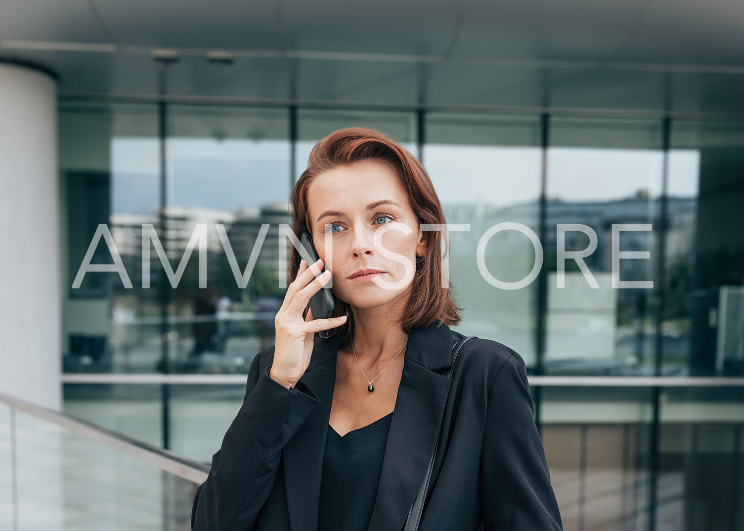 Portrait of a middle-aged female with ginger hair talking on her mobile phone while standing outdoors against a glass building