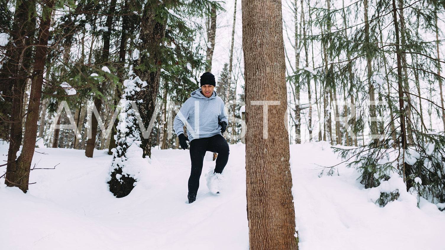 Young man exercising in the forest, running down through a snow	