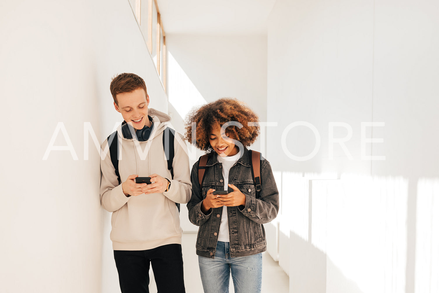 Laughing classmates walking together in corridor holds smartphones