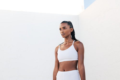 Portrait of a muscular athlete in white fitness attire. Confident sportswoman standing outdoors taking a break.