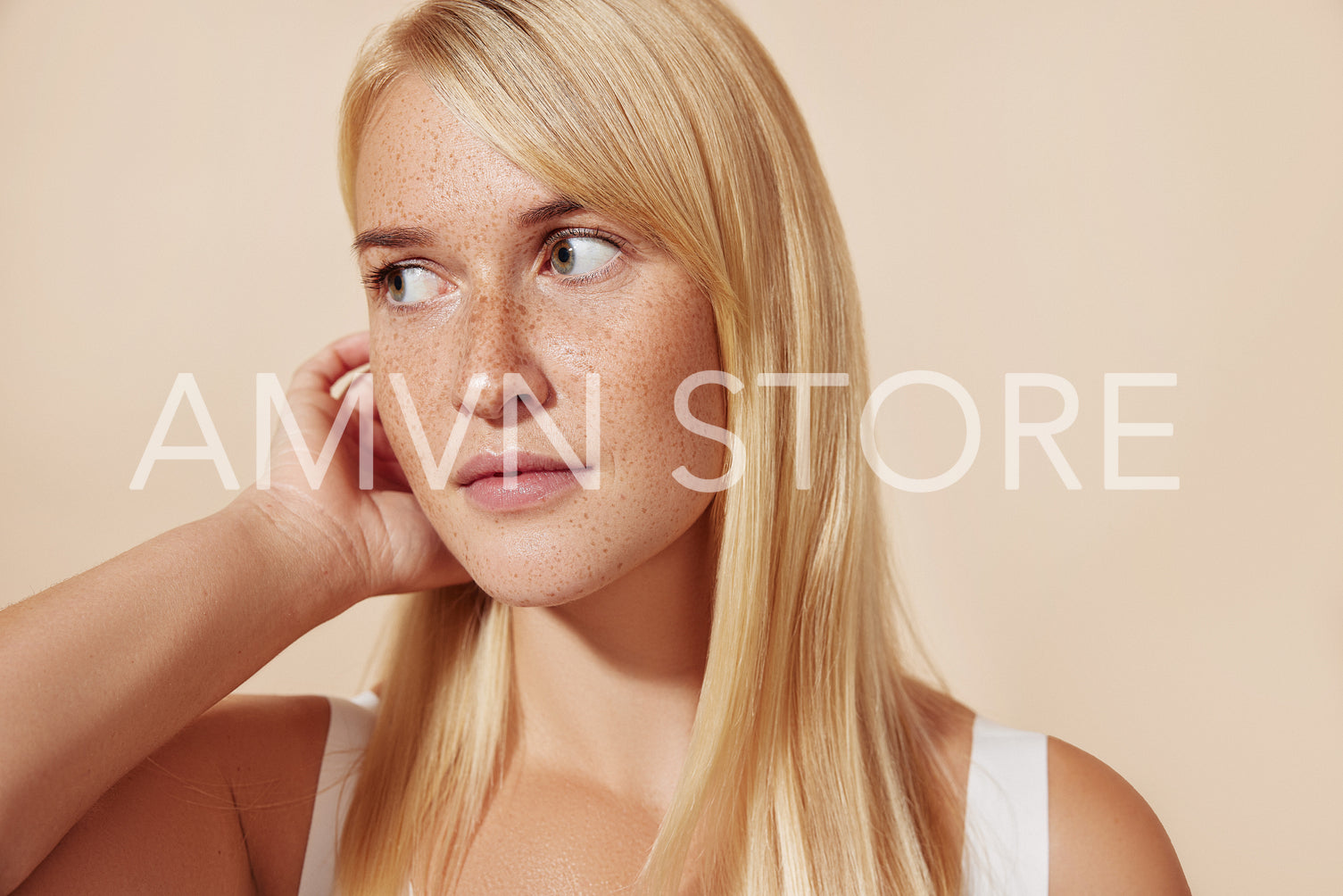 Close-up of freckled female looking away while adjusting her blond hair in studio. Portrait of a beautiful woman with perfect smooth skin.