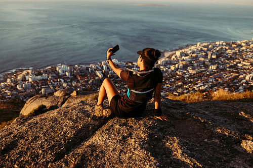 Rear view of female trail runner relaxing on the top of the mountain at sunset