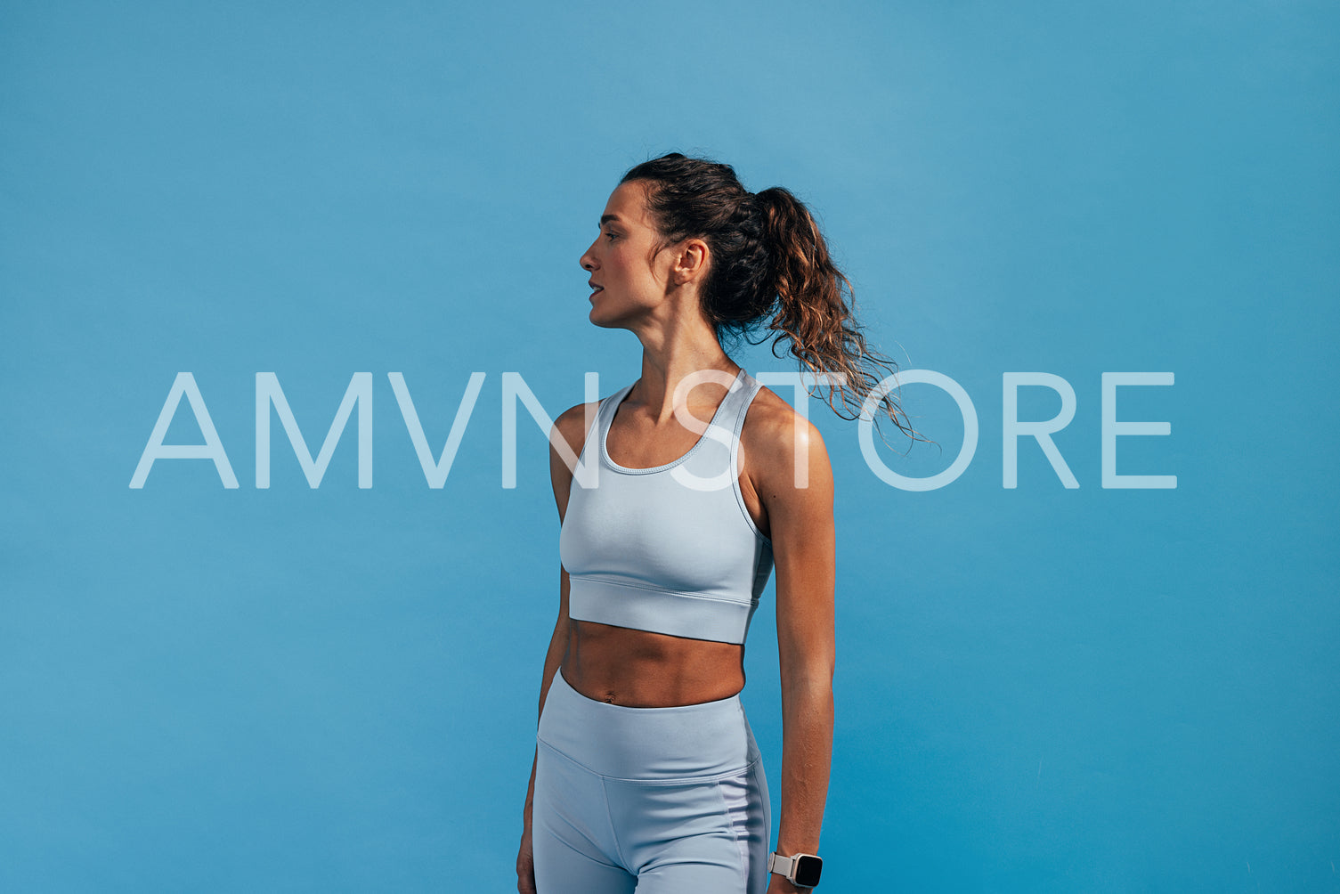 Side view portrait of sportswoman in blue fitness wear. Female athlete standing on blue background.