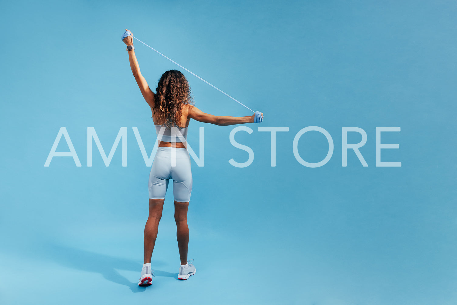 Back view of fit woman standing on blue background doing strength training using resistance bands