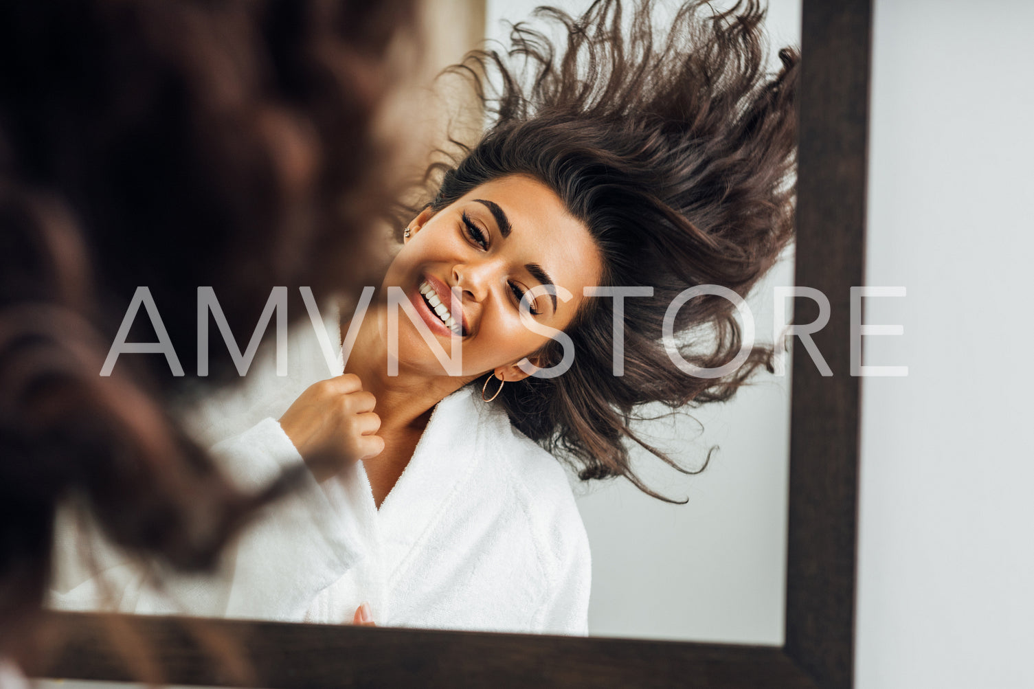 Portrait of a young happy woman playing with her hair in front of a bathroom mirror	