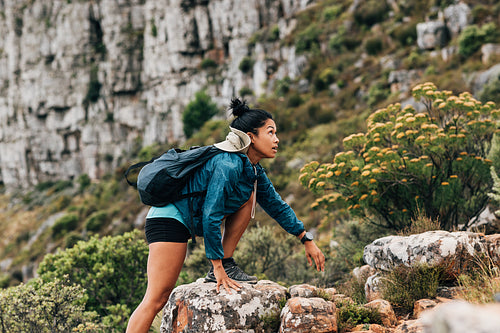 Side view of a woman in sports clothes looking up while climbing up on a rock