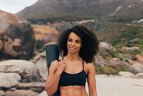 Portrait of a beautiful young woman with curly hair holding a yoga mat while standing outdoors