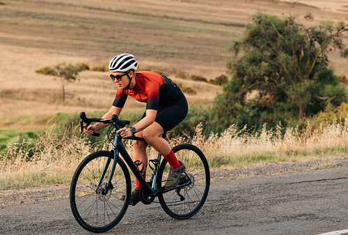 Woman riding a bicycle on empty road. Sportswoman in fitnesswear practicing on pro bike.