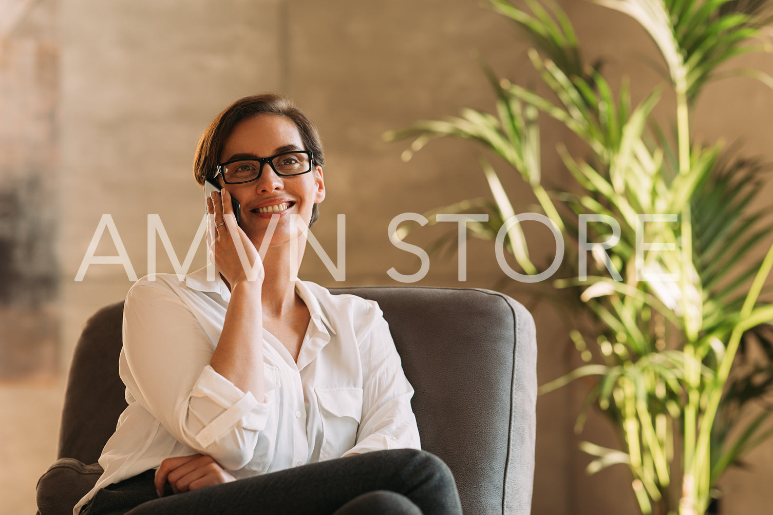 Smiling businesswoman in eyeglasses talking on mobile phone indoors