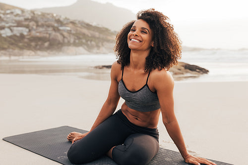 Happy woman in sportswear sitting on beach. Laughing female relaxing after yoga exercises at sunset.