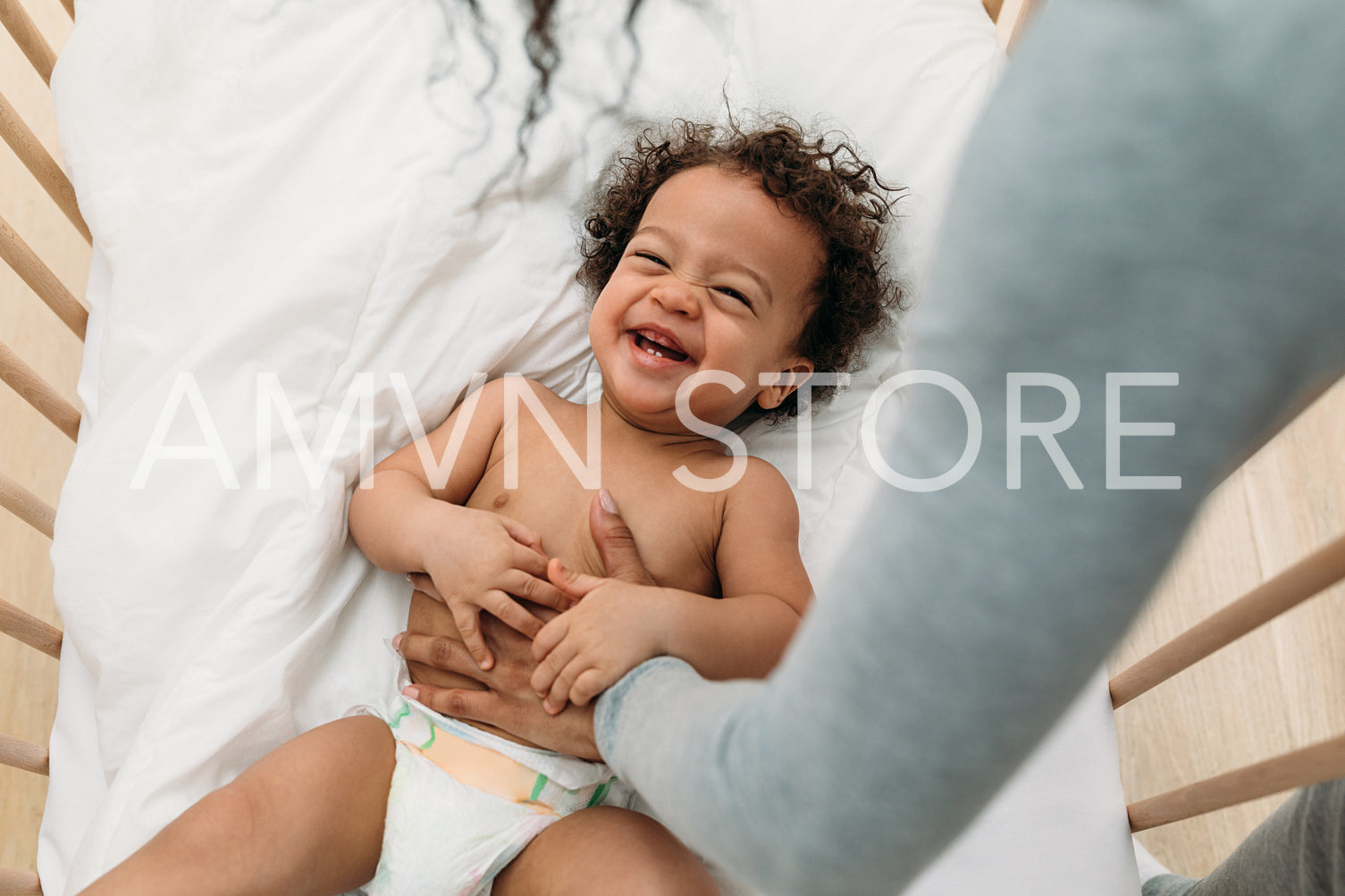 Mother tickling happy baby boy while he lying on crib	