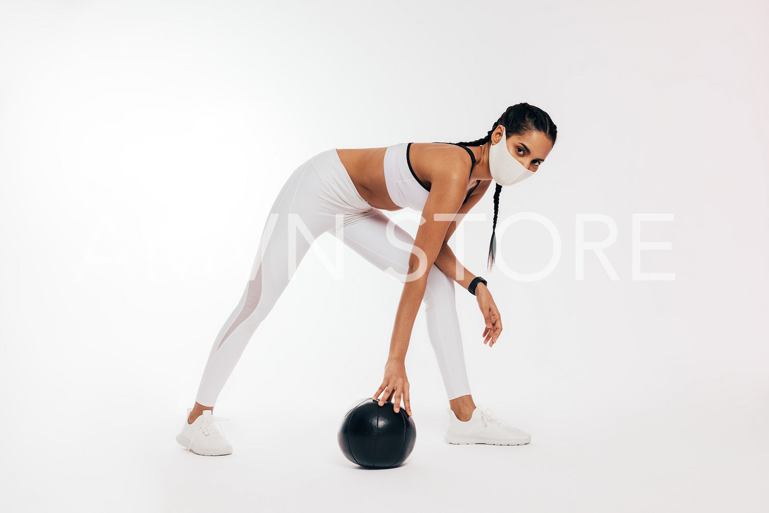 Young woman in sportswear with protective face mask exercising with medicine ball against a white background