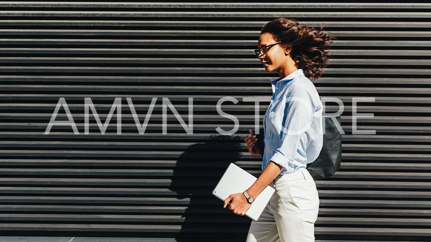 Side view of businesswoman holding a digital tablet, walking outside at wall	