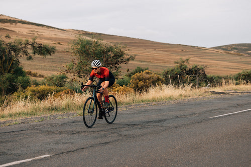 Female cyclist riding her pro bike on empty countryside road on a summer day