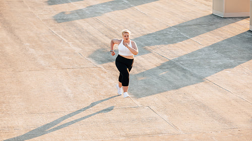 Plus size woman running on a roof. Young oversize female doing cardio training outdoors.