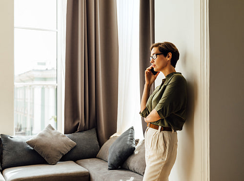 Young businesswoman standing in an apartment at window and making a phone call