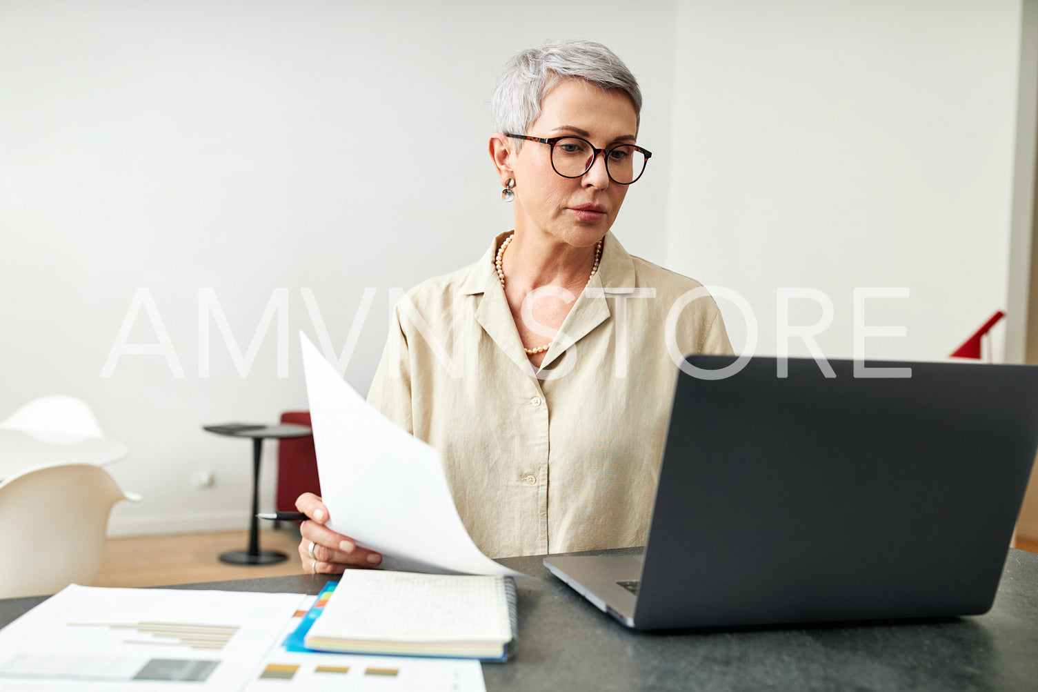 Mature woman with documents using laptop at desk in living room